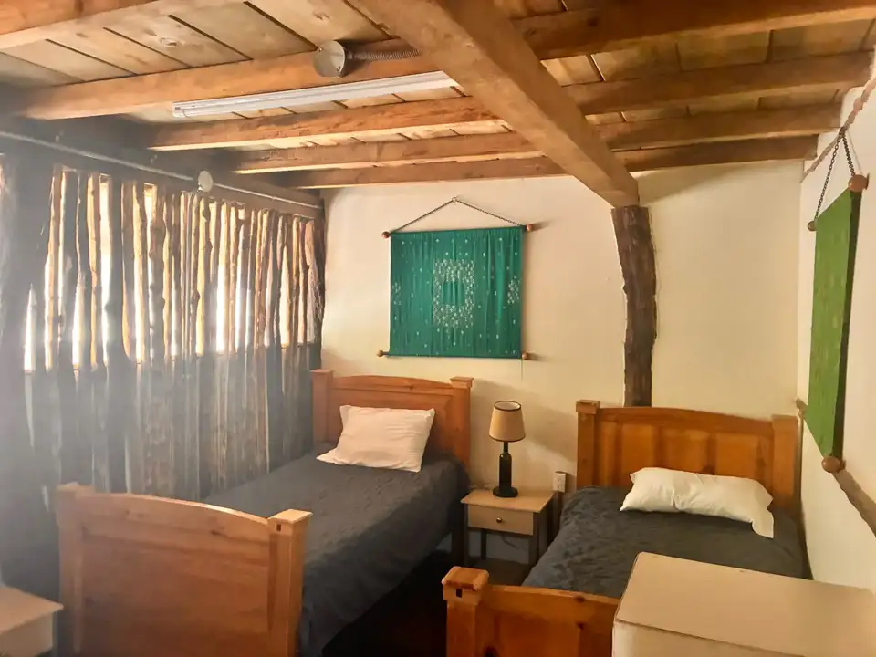 Dormitorio de Aguacatillo con dos camas individuales, vigas de madera y textiles verdes