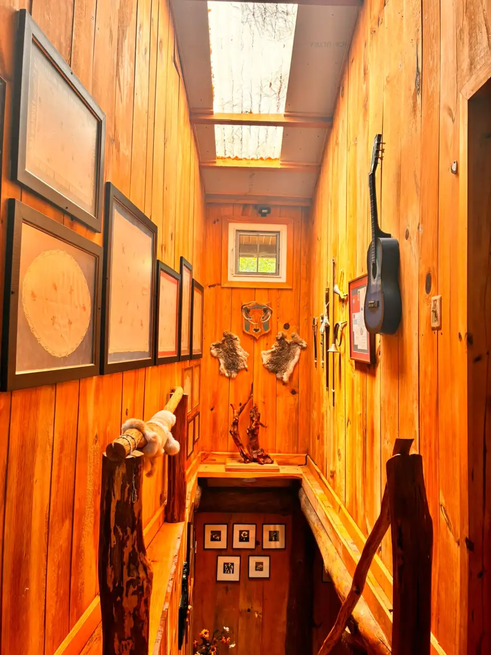Escalera de madera de Platanar con cuadros, guitarra y objetos decorativos bajo un tragaluz