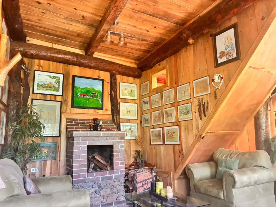 Sala de Platanar con chimenea de ladrillo, sillones, vigas de madera y cuadros
