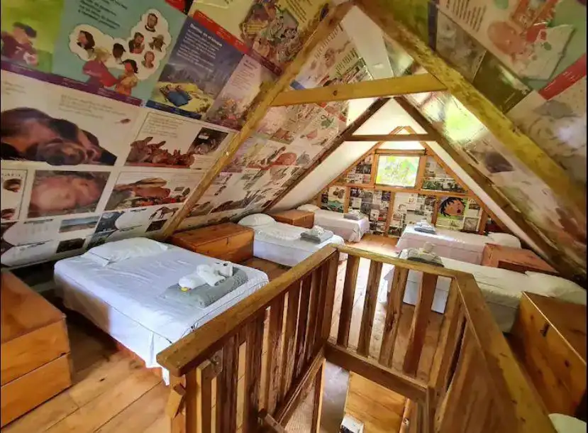 Dormitorio bajo el tejado de Magueyal con varias camas, vigas de madera y paredes cubiertas de arte e ilustraciones